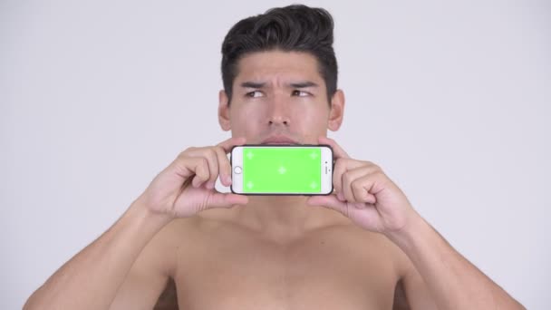 Счастливый молодой мускулистый мужчина без рубашки думает, показывая телефон — стоковое видео