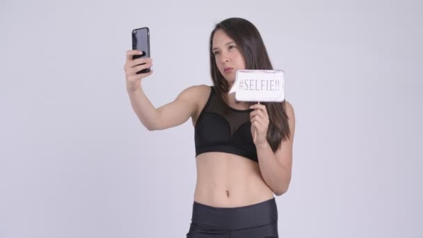 Młoda kobieta wieloetnicznego szczęśliwy, biorąc selfie z papieru znak gotowy na siłowni — Wideo stockowe