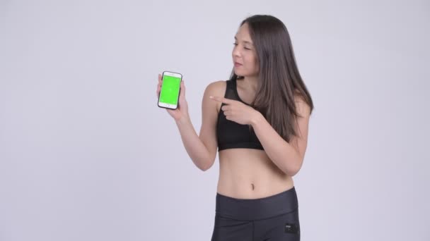Молода щаслива жінка показує телефон і дає великі пальці готові до спортзалу — стокове відео