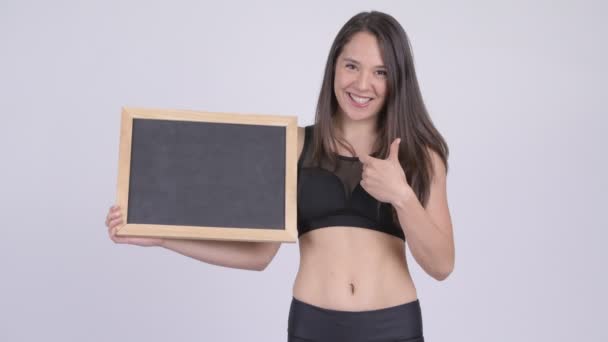 Jovem mulher feliz segurando quadro-negro e dando polegares para cima pronto para ginásio — Vídeo de Stock