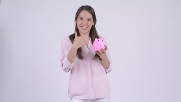 Молодая счастливая многонациональная деловая женщина, держащая копилку и показывающая большие пальцы — стоковое видео