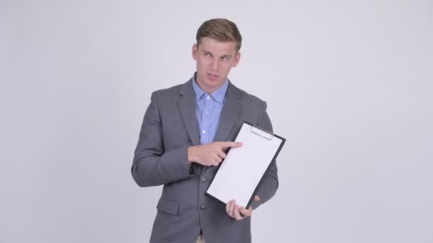 Stressed young businessman showing clipboard and giving thumbs down — Stock Video