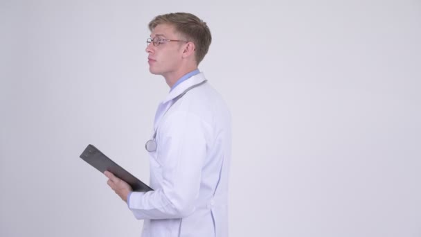 Feliz joven guapo médico hombre sosteniendo portapapeles y saludando de la mano — Vídeos de Stock