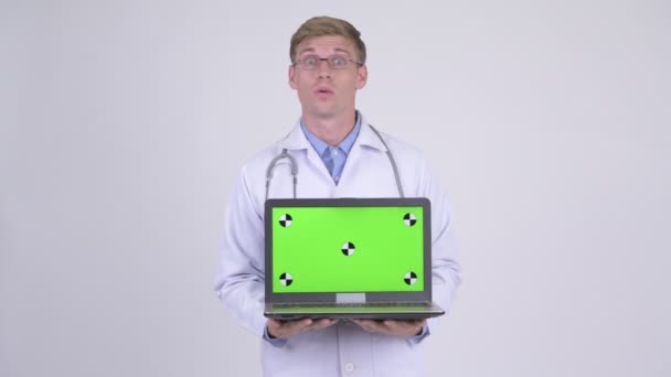 Jovem feliz bonito homem médico pensando ao mostrar laptop — Vídeo de Stock