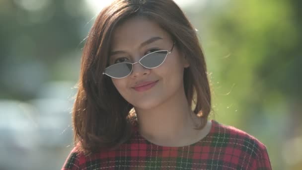 Лицо молодой счастливой азиатской бизнесвумен в солнечных очках улыбается на открытом воздухе — стоковое видео