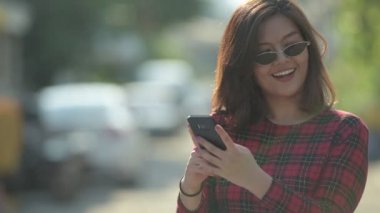Mutlu genç güzel Asya işkadını telefon açık havada kullanırken düşünme
