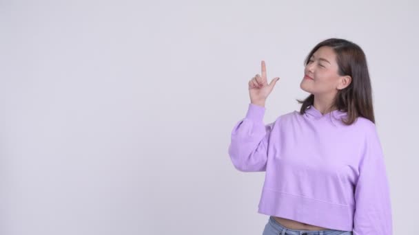 Молодая счастливая азиатка думает и показывает вверх — стоковое видео