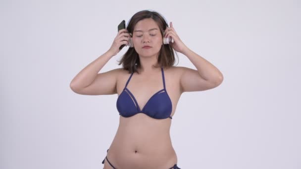 Mladé krásné asijské turistické ženy tančí při používání telefonu a sluchátka — Stock video