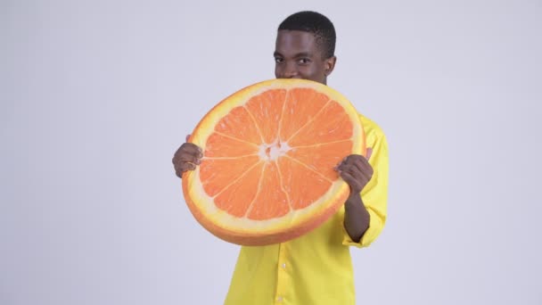 Молодой счастливый африканский бизнесмен кусает апельсиновую подушку как здоровую концепцию — стоковое видео