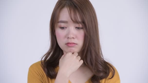 Gezicht van jonge ernstige Aziatische vrouw denken terwijl neer te kijken — Stockvideo