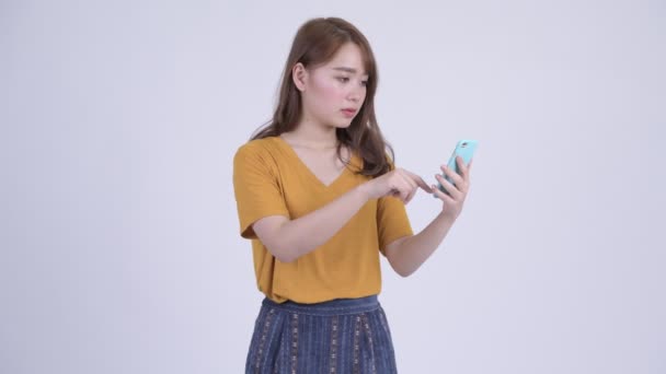 Felice giovane bella donna asiatica utilizzando il telefono e guardando sorpreso — Video Stock