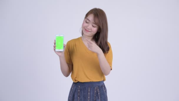 Happy young beautiful Asian woman showing phone and giving thumbs up — Stock Video
