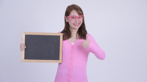 Joven feliz asiática nerd mujer sosteniendo blackboard y dando pulgares arriba — Vídeos de Stock