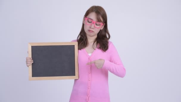 Jovem triste ásia nerd mulher segurando blackboard e dando polegares para baixo — Vídeo de Stock