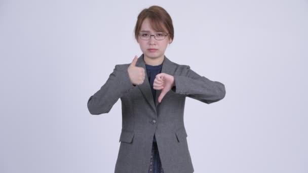 Молодая запутавшаяся азиатская бизнесвумен выбирает между большим и большим пальцами вниз — стоковое видео