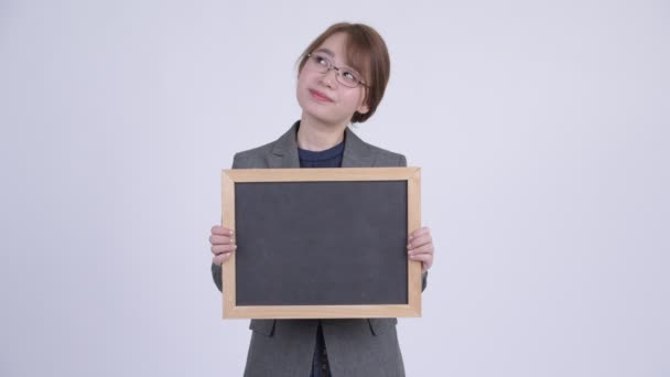 Jovem feliz mulher de negócios asiática pensando enquanto segurando quadro negro — Vídeo de Stock