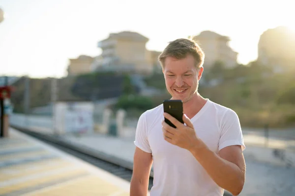Νέοι ευτυχισμένη όμορφος τουριστικά άνθρωπος χρησιμοποιώντας το τηλέφωνο στο σταθμό του τρένου — Φωτογραφία Αρχείου
