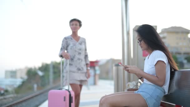 Jovem ásia mulher usando telefone no o trem estação com maduro turista mulher perguntando direções — Vídeo de Stock