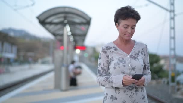 Zralá žena krásné turistické použití telefonu při čekání na vlakovém nádraží — Stock video