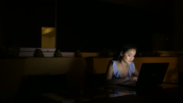 Молода щаслива азіатка використовує ноутбук у темній кімнаті — стокове відео