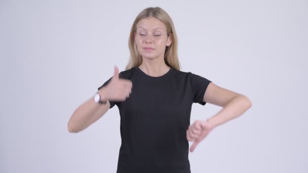 Jonge blonde vrouw kiezen tussen duim omhoog verward en duim omlaag — Stockvideo