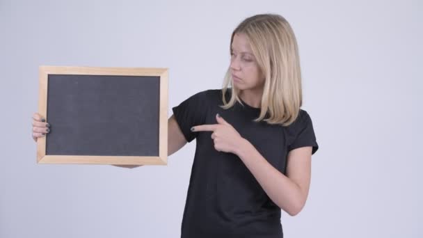 Young serious blonde woman holding blackboard and giving thumbs down — Stock Video