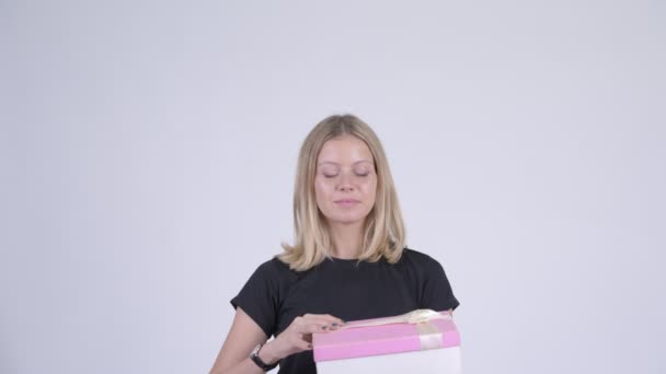 Молода щаслива блондинка відкриває подарункову коробку і виглядає здивованою — стокове відео