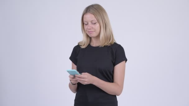 Молодая счастливая блондинка улыбается во время использования телефона — стоковое видео