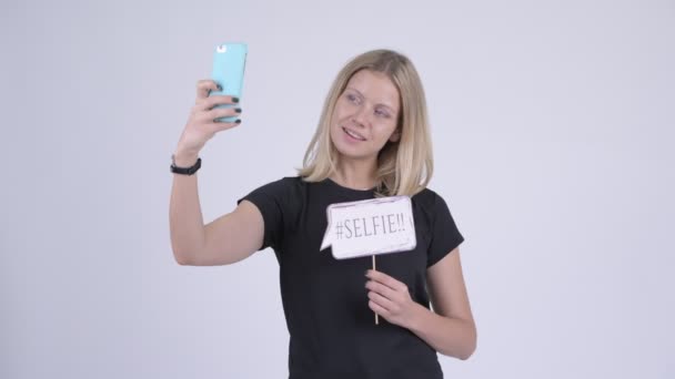 Молода щаслива блондинка бере селфі з паперовим знаком — стокове відео
