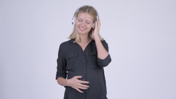 Молодая счастливая беременная деловая женщина думает, слушая музыку — стоковое видео
