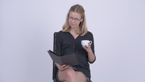 Junge glückliche schwangere Geschäftsfrau sitzt beim Lesen von Büchern und Kaffee trinken — Stockvideo