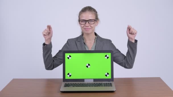 Joven mujer de negocios rubia feliz mostrando portátil y dando pulgares en el escritorio — Vídeo de stock