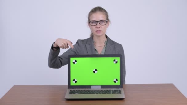 Junge glückliche blonde Geschäftsfrau zeigt Laptop und präsentiert etwas am Schreibtisch — Stockvideo