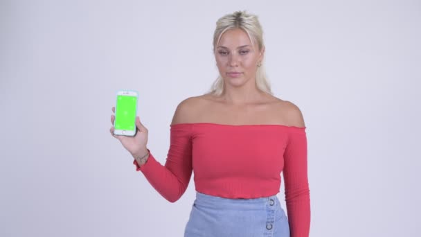 Gelukkig jonge mooie blonde vrouw tonen van de telefoon en geven duimen omhoog — Stockvideo