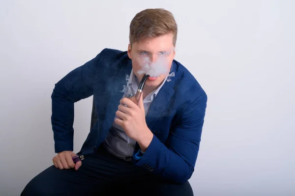 Молодой привлекательный блондин-бизнесмен сидит во время курения трубку — стоковое фото
