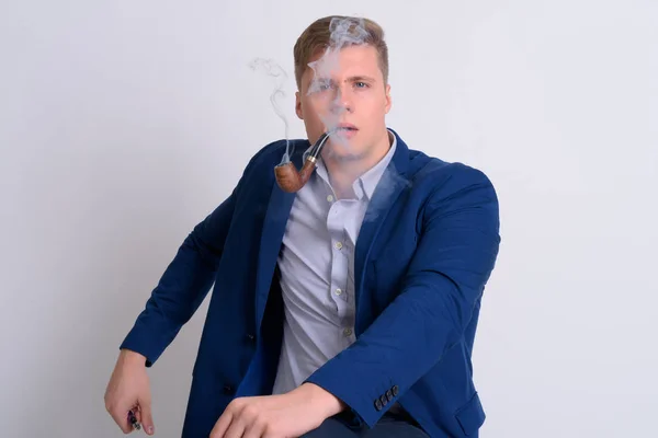 Joven guapo hombre de negocios rubia sentado mientras fuma pipa —  Fotos de Stock