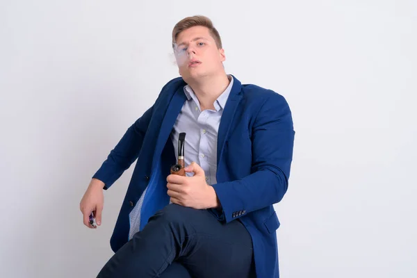 Joven guapo hombre de negocios rubia sentado mientras fuma pipa —  Fotos de Stock