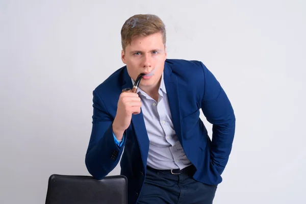 Joven guapo rubia hombre de negocios fumar pipa mientras se apoya en silla — Foto de Stock