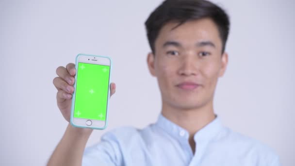 Face of young happy Asian businessman showing phone — Stock Video