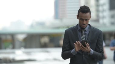 Telefon açık havada kullanırken mutlu genç Afrikalı işadamı düşünme