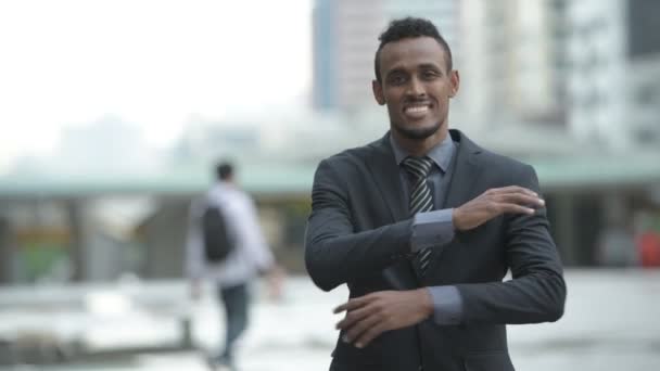 Счастливый молодой африканский бизнесмен улыбается, скрестив руки в городе на улице — стоковое видео