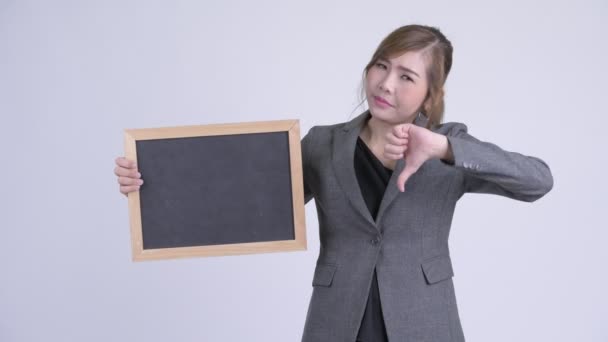Young stressed Asian businesswoman holding blackboard and giving thumbs down — Stock Video