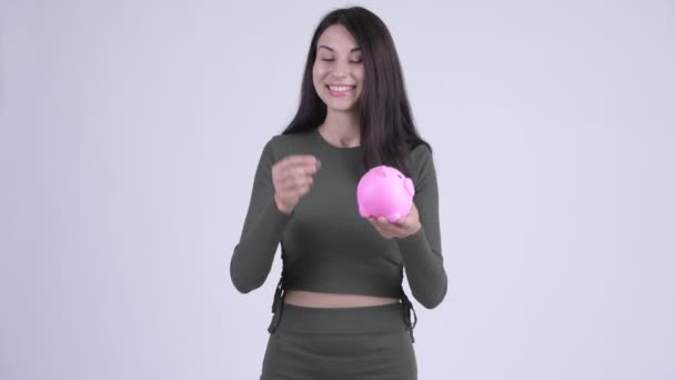 Glückliche junge schöne Frau, die Münze in Sparschwein als Witz einwirft — Stockvideo