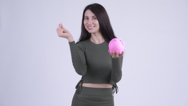 Счастливая молодая красивая женщина вставляет монету в копилку — стоковое видео
