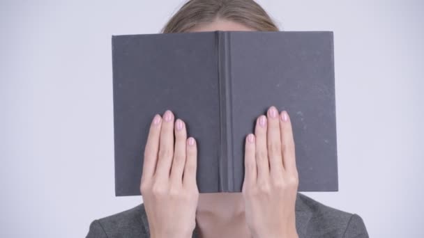 Gesicht einer jungen schüchternen blonden Geschäftsfrau, die ihr Gesicht mit einem Buch verhüllt — Stockvideo