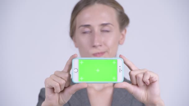 Ansikte av glad ung blond affärskvinna tänkande samtidigt visar telefonen — Stockvideo