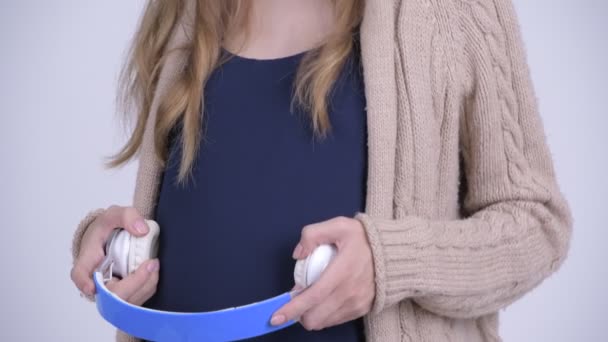 Счастливая молодая красивая беременная женщина с наушниками на животе — стоковое видео