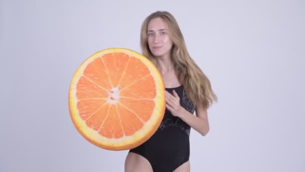 Happy young blonde woman in swimsuit biting orange pillow as healthy concept — Stock Video