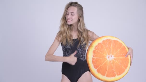 Joven mujer feliz en traje de baño dando pulgares hacia arriba con almohada naranja como concepto saludable — Vídeo de stock