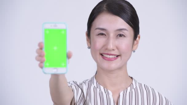 Лицо счастливой красивой азиатской бизнесвумен показывая телефон — стоковое видео